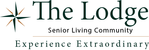 Logo of "The Lodge" senior living community. Features a green and orange compass star on the left, with the text "The Lodge" in large font, "Senior Living Community" below it, and "Experience Extraordinary" at the bottom.