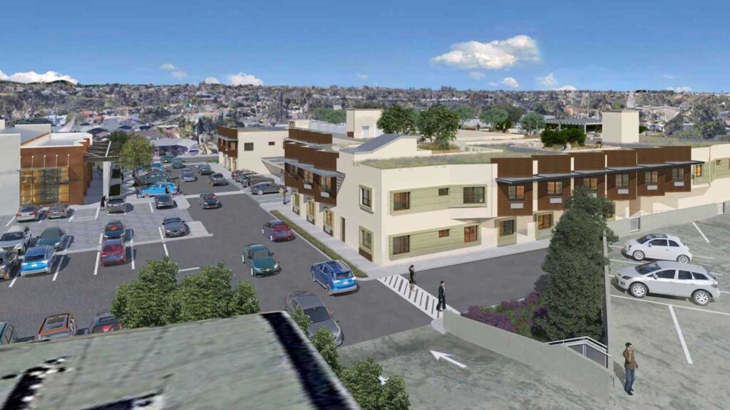 Aerial view of a modern urban area with two-story buildings featuring rooftop greenery. Several parked cars fill the adjacent parking lot. A few pedestrians are walking near the buildings under a clear blue sky with scattered clouds.